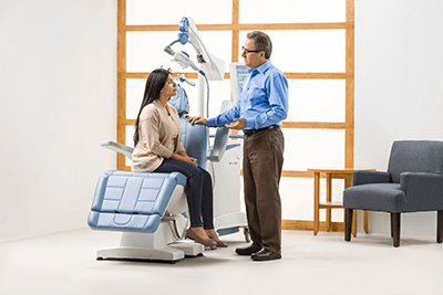 Picture of woman wearing a brown shirt sitting down on a NeuroStar TMS Machine discussing treatment with a doctor