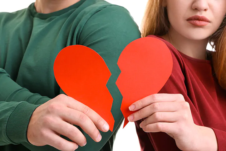 man and woman standing back to back each holding half of a torn paper heart for the article Common Mistakes that Destroy Relationships