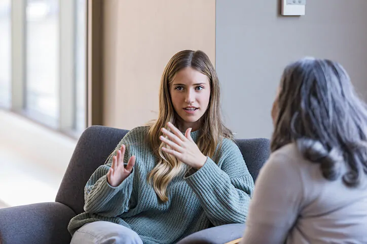 Young blond girl in green sweatshirt discussing Treating Depression & Anxiety with Logic with older female therapist wearing a long sleeve blouse.