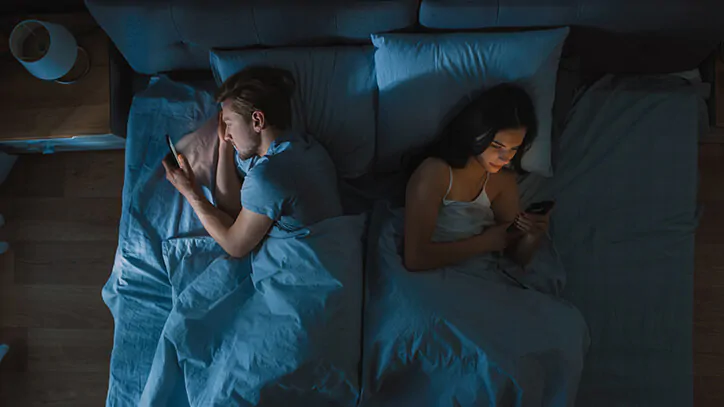 Young couple in bed with backs to each other while using cell phones